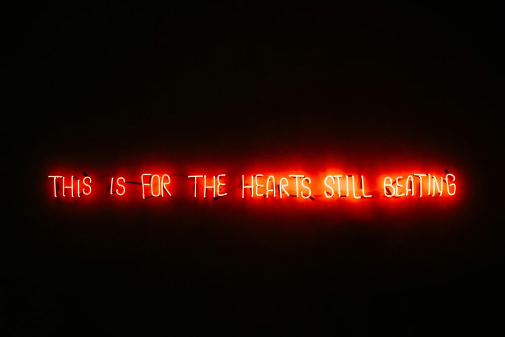 Red neon sign glowing with the message "This is for the hearts still beating" on a dark background.